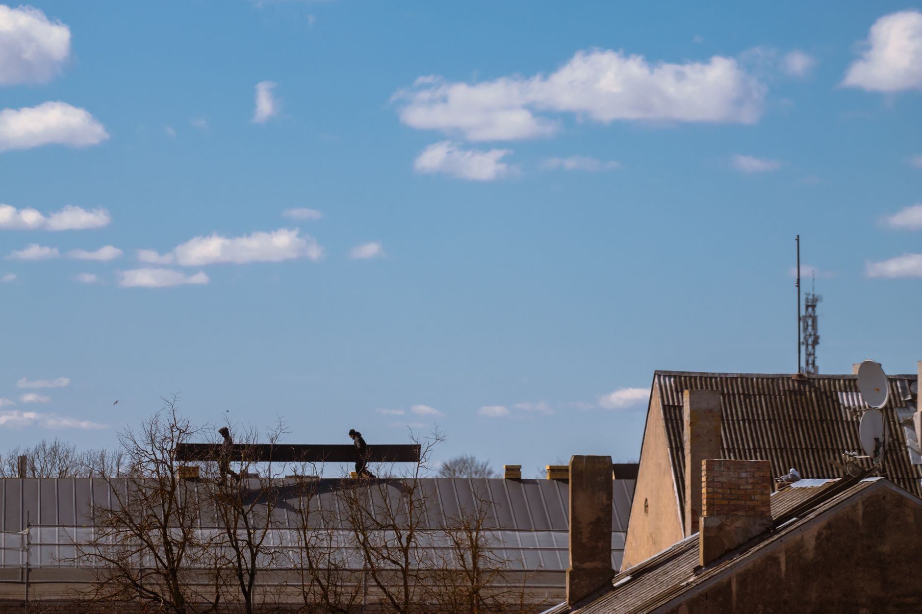 Silhouetted workers on a roof against a blue sky